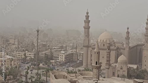 Bird's eye view of ancient Islamic architecture in Cairo, Egypt, featuring the iconic Sultan Hassan Mosque complex with minarets, domes and medieval stone walls.