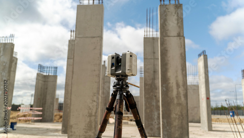 Photos Surveying equipment stands before unfinished concrete pillars