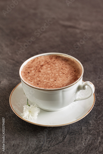 A steaming cup of cappuccino on a dark wooden surface	