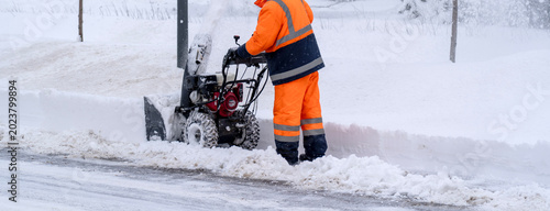 Worker clears snow with machine on icy road