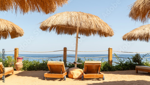 Фотография Sunlit beach with straw umbrellas and wooden loungers