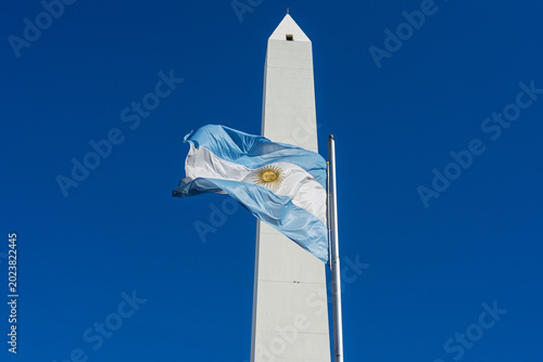 Fotografie National flag of Argentina waving in front of the iconic Obelisk monument agains