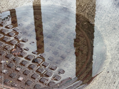 Puddle on manhole cover with reflection of urban environment