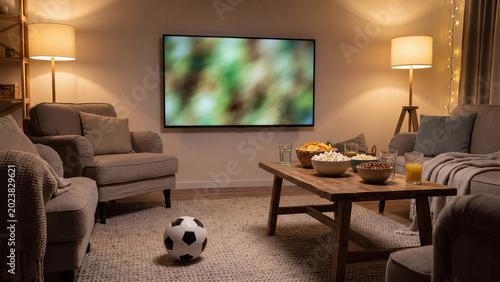 Cozy football watch party at home with soccer ball, snacks and big screen TV in living room, warm family entertainment concept for match night, sports viewing and game day celebration
