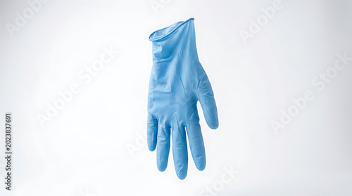 Single blue nitrile medical examination glove floating on a white background representing hygiene, safety, and infection control in professional dental and healthcare environments and surgery.