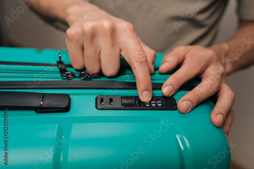 Фотография Male traveler hands meticulously adjusting the numbers on a built-in combination lock of a turquoise suitcase, preparing for travel, securing contents, or arriving home from a journey