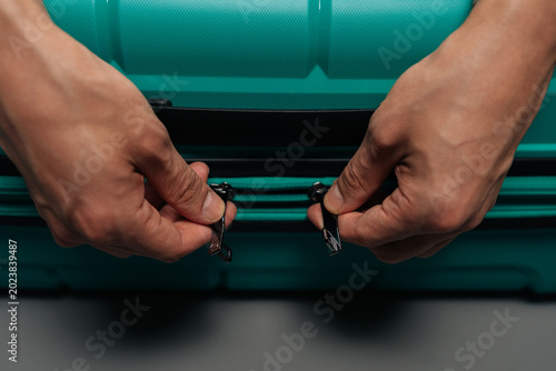 Bild auf Leinwand Two hands zipping a turquoise suitcase, preparing for a trip, packing luggage, or unpacking after travel, symbolizing journey, adventure, and personal belonging management