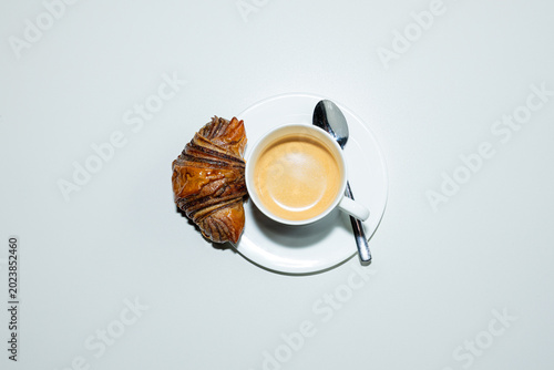 Top down view of a creamy espresso and a mini croissant