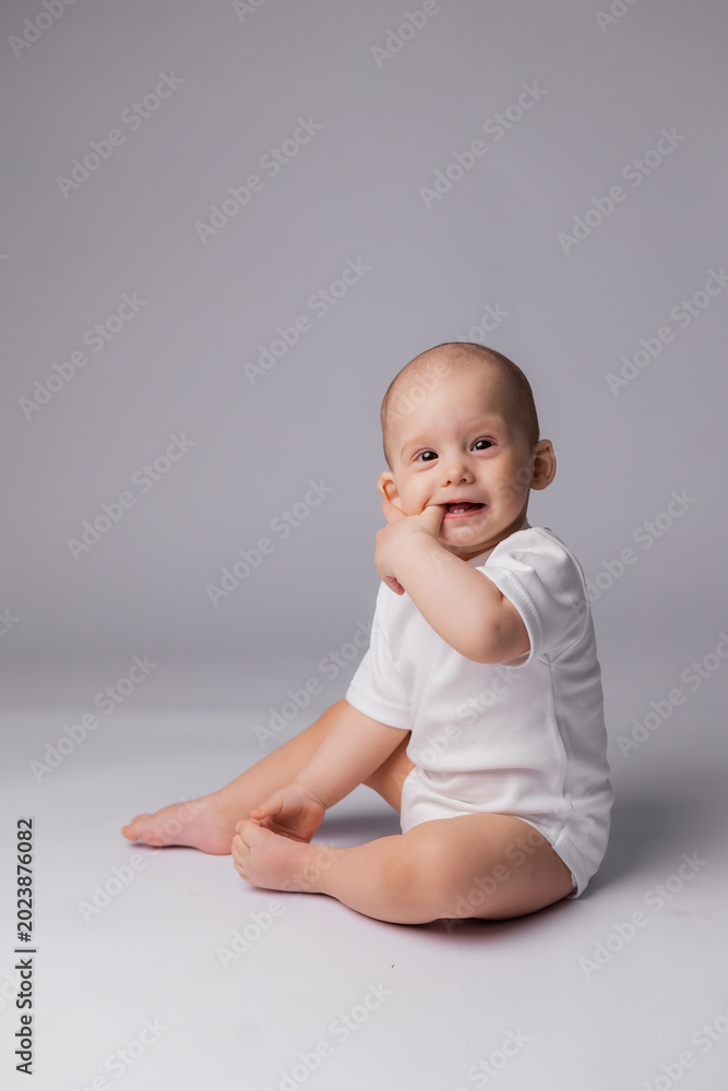 Fototapeta premium baby in a white bodysuit is sitting on a white background in the studio