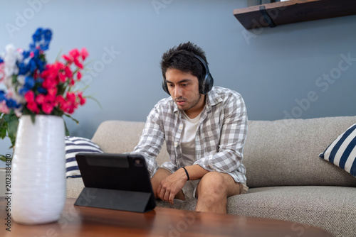 Canvas Print Young man concentrating watching tablet wearing headphones at home