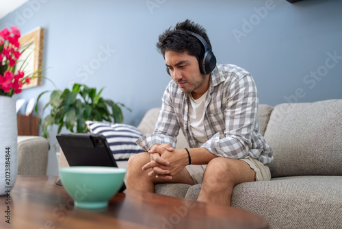 Bild auf Leinwand Young man concentrating on tablet with headphones at home