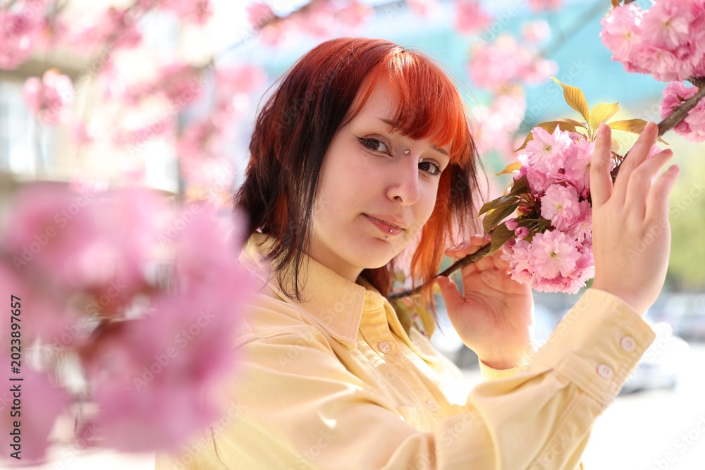 Fototapeta premium Beautiful young girl posing near blossoming sakura tree outdoors