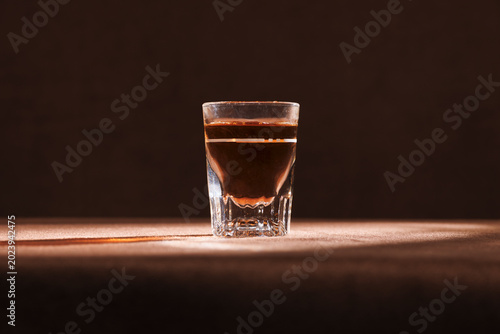 One simple shot of dark liquor like whiskey or brandy with a dark background on a tablecloth