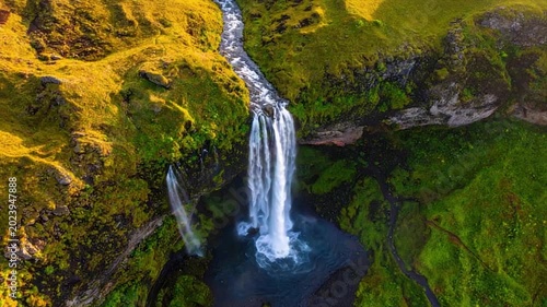 Aerial view of a waterfall cascading down a lush green hillside, creating a pool below