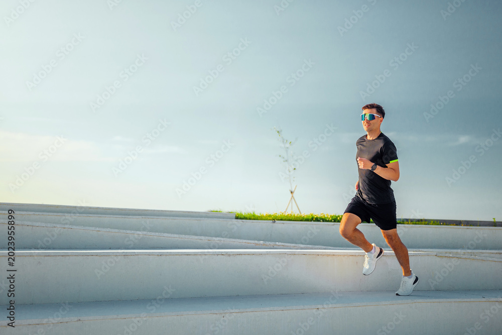 Fototapeta premium Young man runs energetically on outdoor steps during a sunny morning in a tranquil urban park