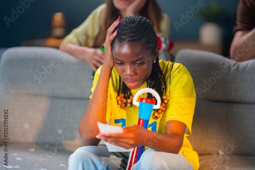 Fotografija Frustrated football supporter looking at a betting slip after a disappointing soccer match moment during an emotional watch party at home