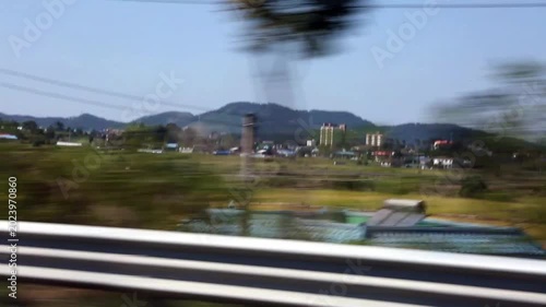 자동차 창밖 풍경 농촌 마을 논밭 자연 서울: 대한민국 서울 교외의 도로를 달리는 차량 안에서 촬영한 창밖 전경입니다. 도로변 가드레일 너머로 넓게 펼쳐진 초록색 논밭, 비닐하우스, 평화로운 농촌 마을과 산세를 패스바이 형식으로 담아냈으며, 전원 풍경, 드라이브 여행, 속도감 및 한국의 아름다운 자연 경관을 상징하는 실외 영상입니다.