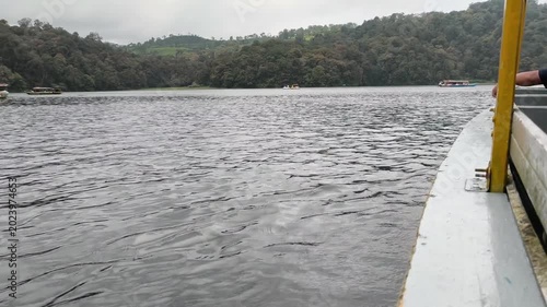 Wide shot of a quiet lake with textured water waves and tree-covered hills in the background. Cloudy weather creates a serene and moody atmosphere