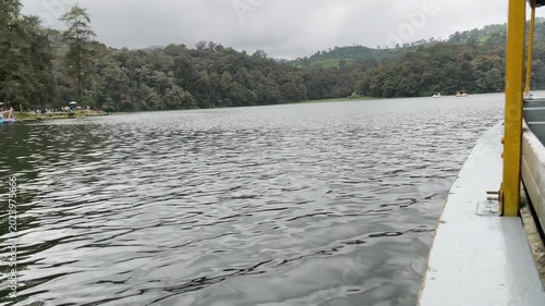 Wide shot of a quiet lake with textured water waves and tree-covered hills in the background. Cloudy weather creates a serene and moody atmosphere