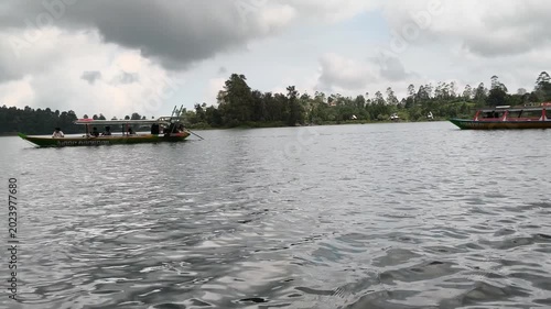 Lake scenery with a floating house or boat visible near the forested shoreline. Gentle water movement and natural surroundings create a relaxing outdoor setting