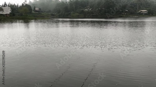 Foggy lake landscape with mist covering distant hills and trees. Moody weather conditions create a cinematic and atmospheric nature scene