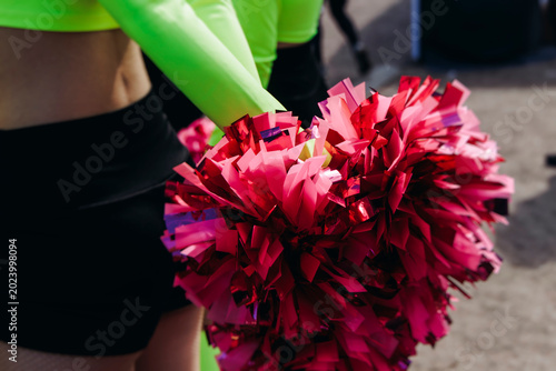 Female cheerleaders group in action, pink and green uniform with pom-pom, audience and sport teams in the background, performing and supporting during outdoor game match, cheerleading on stadium