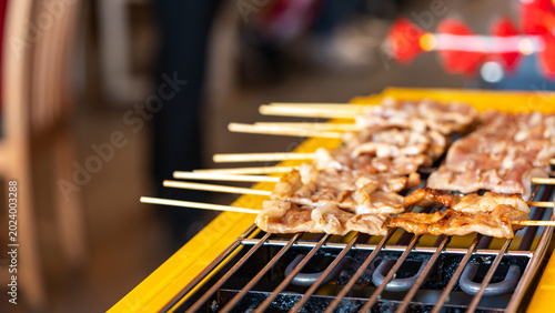 Bild auf Leinwand The shot of a cook grill Moo Ping or grilled pork skewers in Thai style on the yellow electric barbeque grill at the restaurant