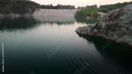 Drone footage flying smoothly over calm turquoise water of a flooded quarry canyon.