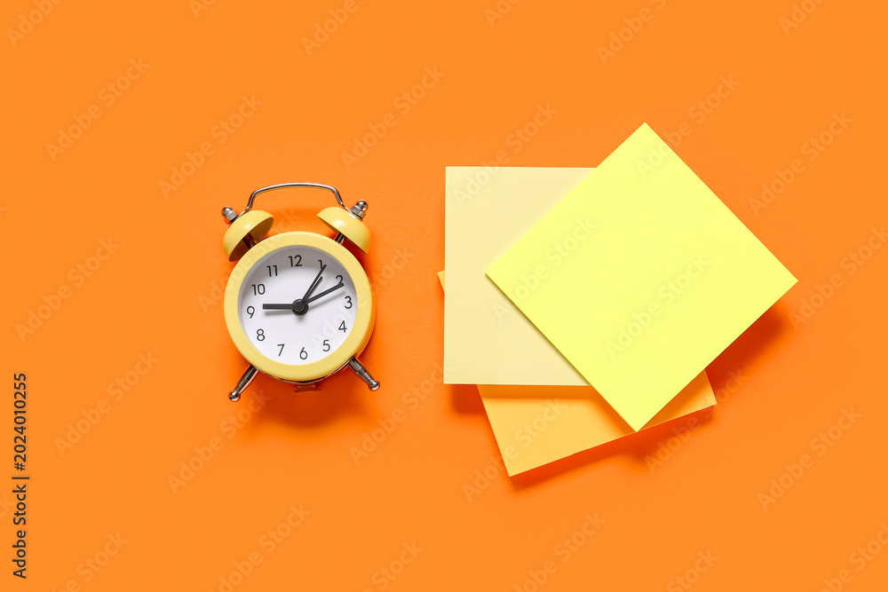 Fototapeta premium Alarm clock with sticky notes on orange background. Time management concept