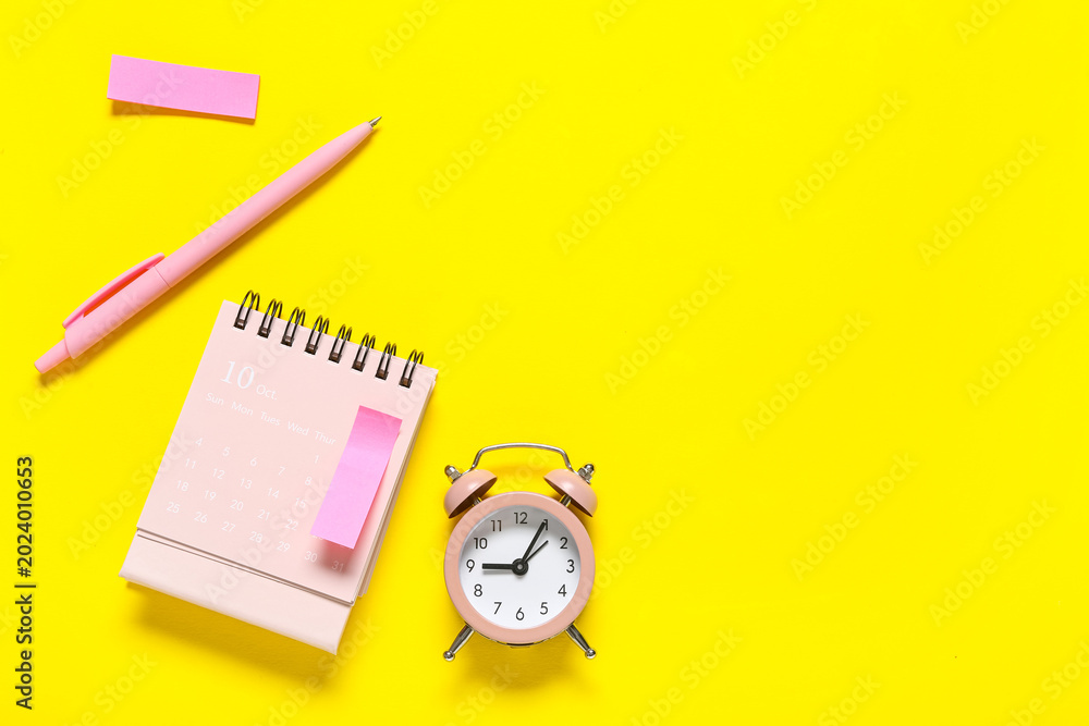 Fototapeta premium Alarm clock with calendar and sticky note on yellow background. Time management concept