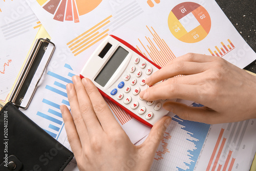 Woman using calculator with diagrams on dark background, closeup. Payment of ...