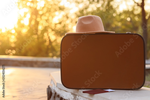 Tableau sur toile Suitcase with passport and hat on parapet in autumn park, closeup