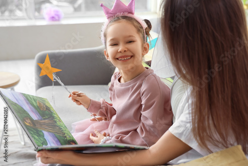Little girl dressed as fairy with her mother reading story at home