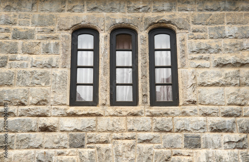 three narrow arched black windows on rustic stone wall, side view of vintage residential building with copy space