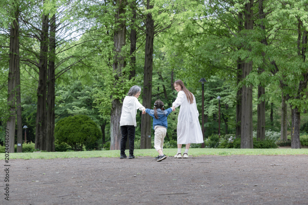 Fototapeta premium 春の新緑の公園で遊ぶおばあちゃんとお母さんと手を繋ぐ歩く寄り添う全身の後ろ姿顔無し 広角全身