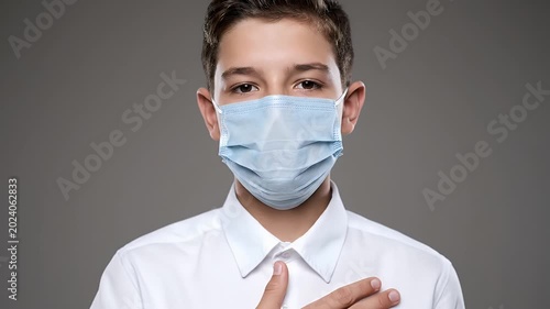 Young boy wears blue medical mask and white shirt showing stop gesture against gray background pandemic prevention