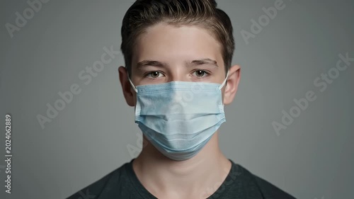 Young Male Wearing Blue Medical Face Mask Against Gray Studio Background with Textured Hair and Dark T Shirt