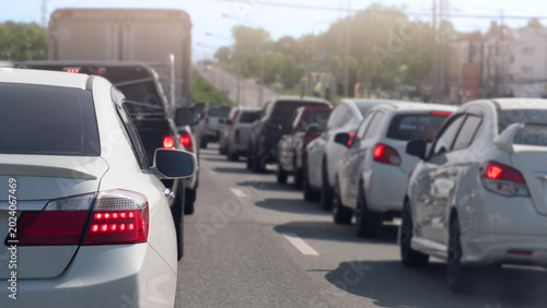 Long line of cars stuck in a traffic jam on a bright day. Perspective is from behind a white sedan. Showing the vast number of vehicles extending into the distance on a multi-lane road.