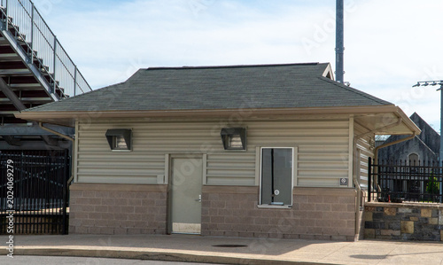 Fotografi Exterior view of a beige and block building, likely a concession stand or ticket booth, at a sports stadium with bleachers, a light pole, and blue sky overhead, perfect for events and outdoor venues