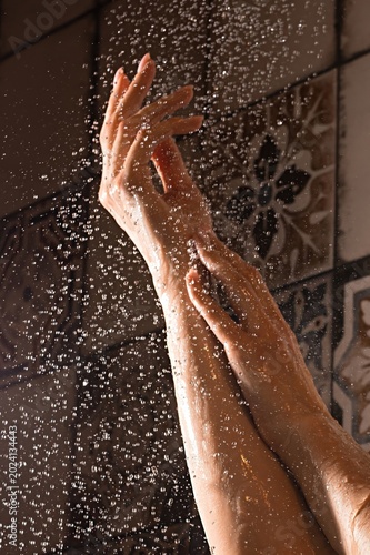 Woman's hands under shower water in bathroom at daytime