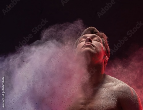 Strong man exhaling colored powder with intensity during a fitness session