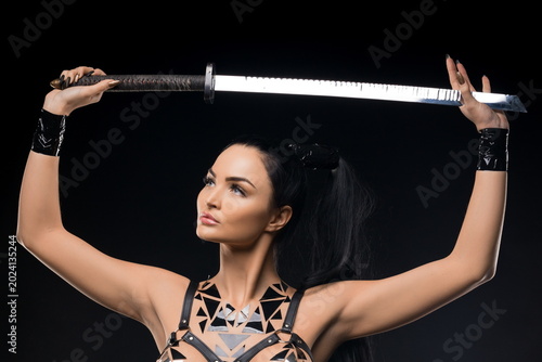 Woman with sword raised above head in dark studio