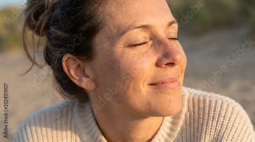 A woman with her eyes closed, basking in the warm sunlight on a beach.