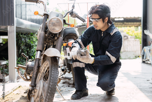 Garage mechanic male worker checkup, fix, replace, service old motorcycle motor bike in workshop.