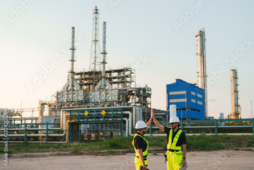 Oil and gas refinery in petroleum industry, industrial plant, refinery worker, high five, safety helmet, safety vest, oil refinery