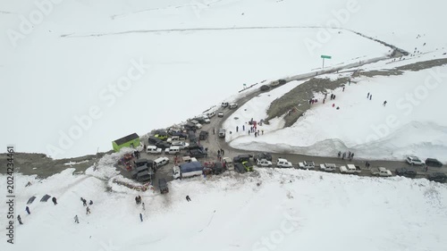 Aerial dronie shot flying away from crowd of people and 4X4 car bus parking to show snow covered surroundings winding roads and mountains of Shinkula top pass in Sissu Ladakh Himachal Pradesh