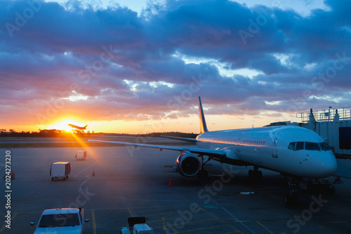Airplane Parked at Airport Gate with Golden Sunrise and Departing Aircraft