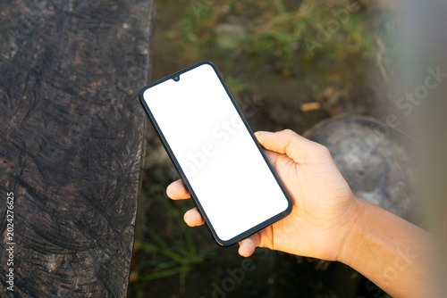 Hand holding smartphone mockup on wooden table with blank screen for mobile app presentation, branding, and digital marketing concepts.