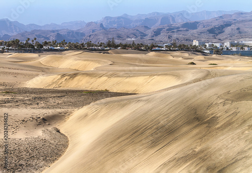 Scenic desert landscape of rolling sand dunes with distant mountains and coastal resort area in Maspalomas, Gran Canaria, Spain.