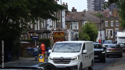 Street-level footage capturing a suburban area in London, England. The scene features residential streets, houses, parked cars, and everyday neighborhood surroundings.